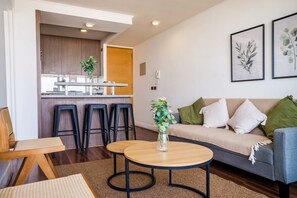 A modern living room with a sofa, two round tables, and a kitchen area in the background. - Chic 2 Bedroom Apartment for 3 with Pool And Gym (Las Condes)