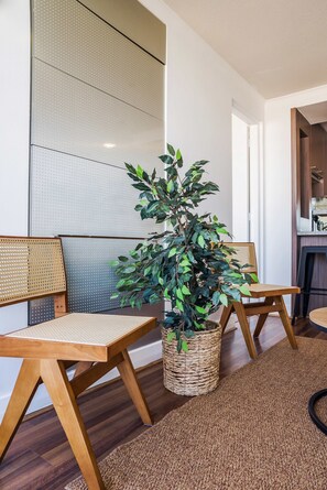 A modern interior with a seating area featuring two wooden chairs with woven seats and backs, a woven floor rug, and a potted plant with green leaves. - Bright 1BR Las Condes  Apartment in Prime location (Las Condes)