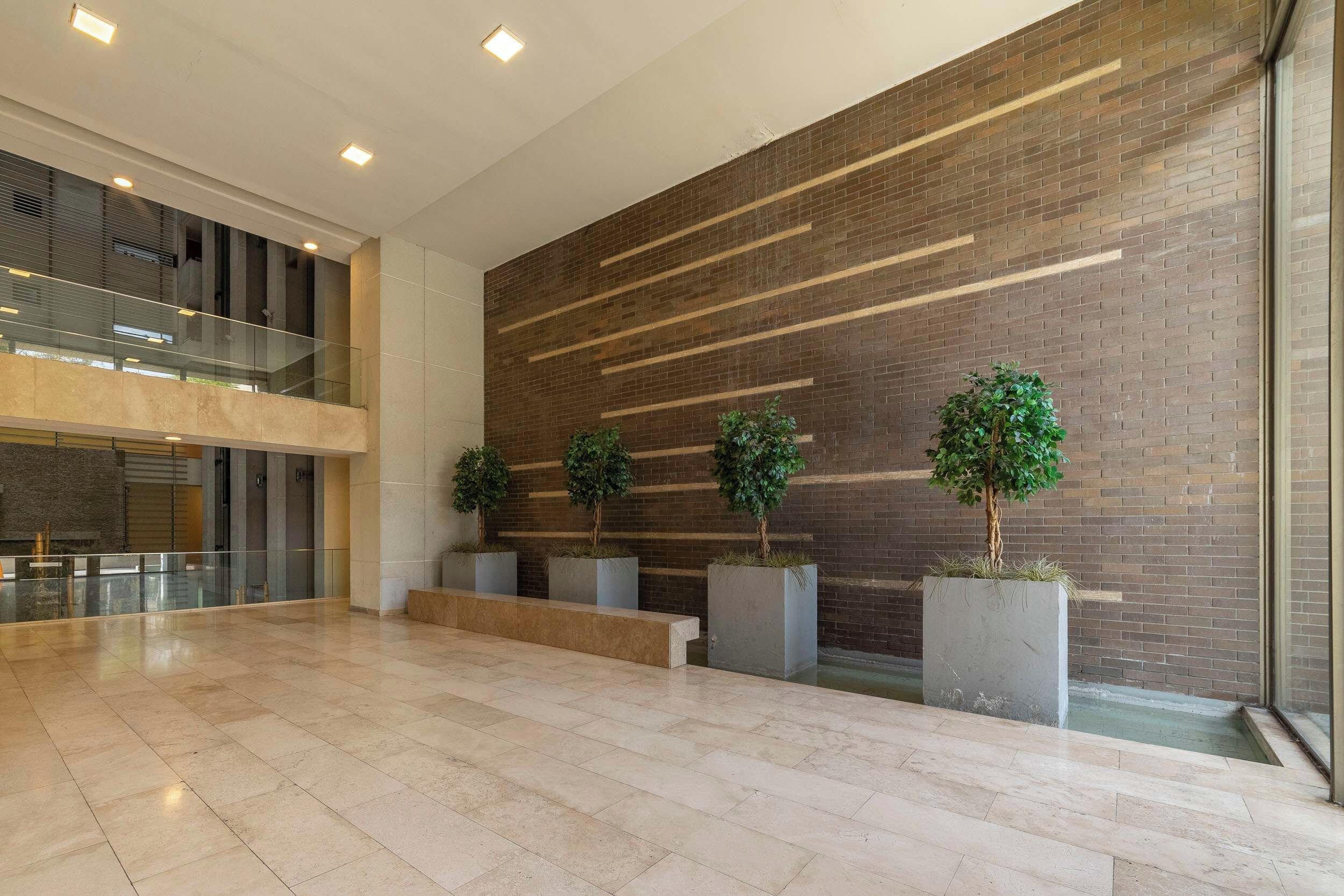 Un hall d’entrée spacieux au design moderne, avec un mur en briques, une rambarde en verre et des plantes en pot.