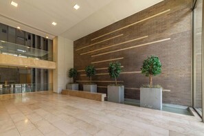 A spacious lobby with a modern design, featuring a brick wall, a glass railing, and potted plants. - Bright 1BR Las Condes  Apartment in Prime location (Las Condes)