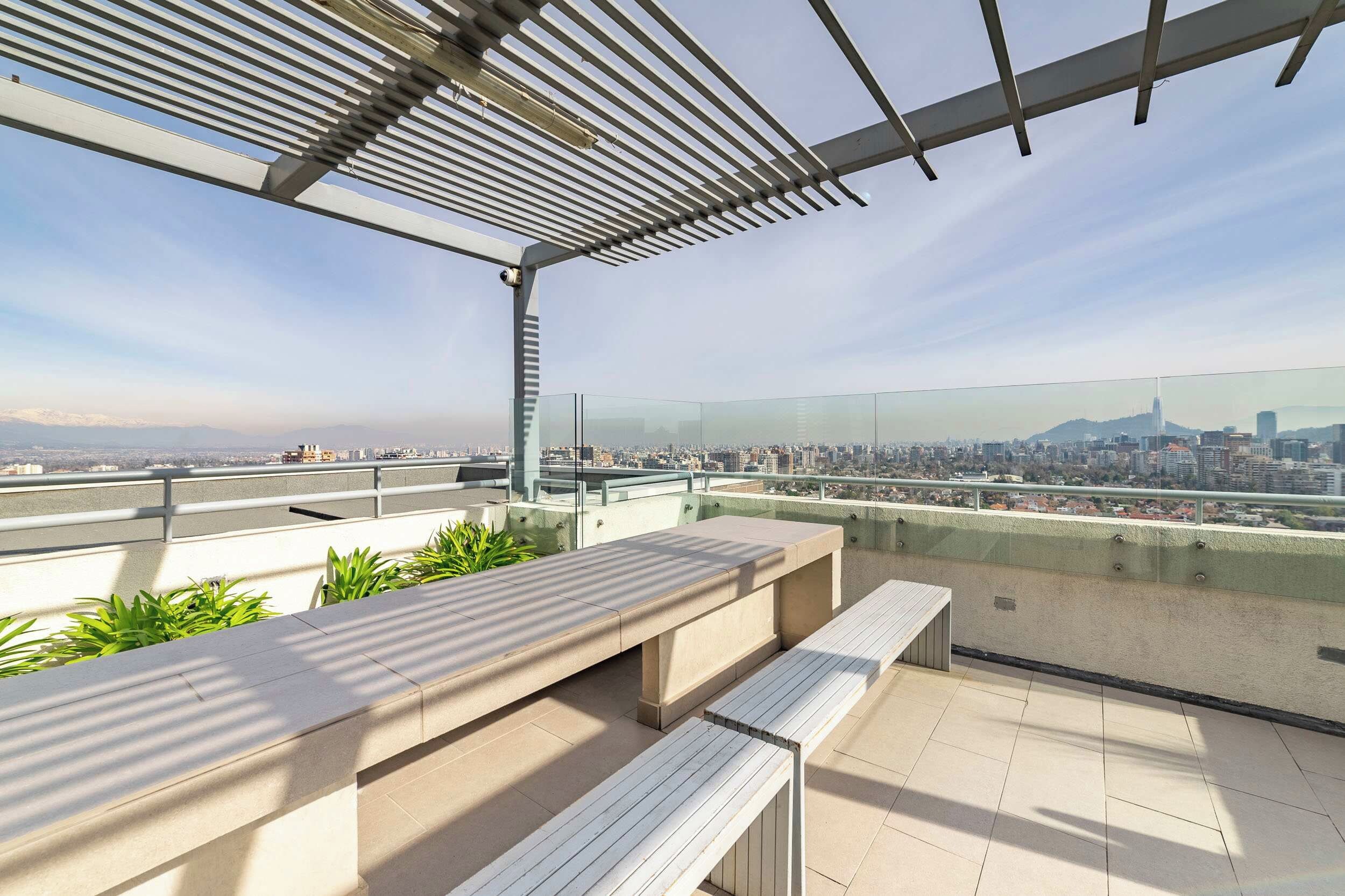 En takterrass med utsikt över stadens silhuett, med en pergola i metall och sittplatser.