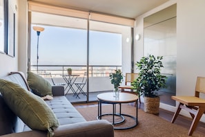 A modern living room with a sofa, a round table, a chair, and a large potted plant. - Chic Las Condes Apartment: Pool & Mountain Views (Las Condes)