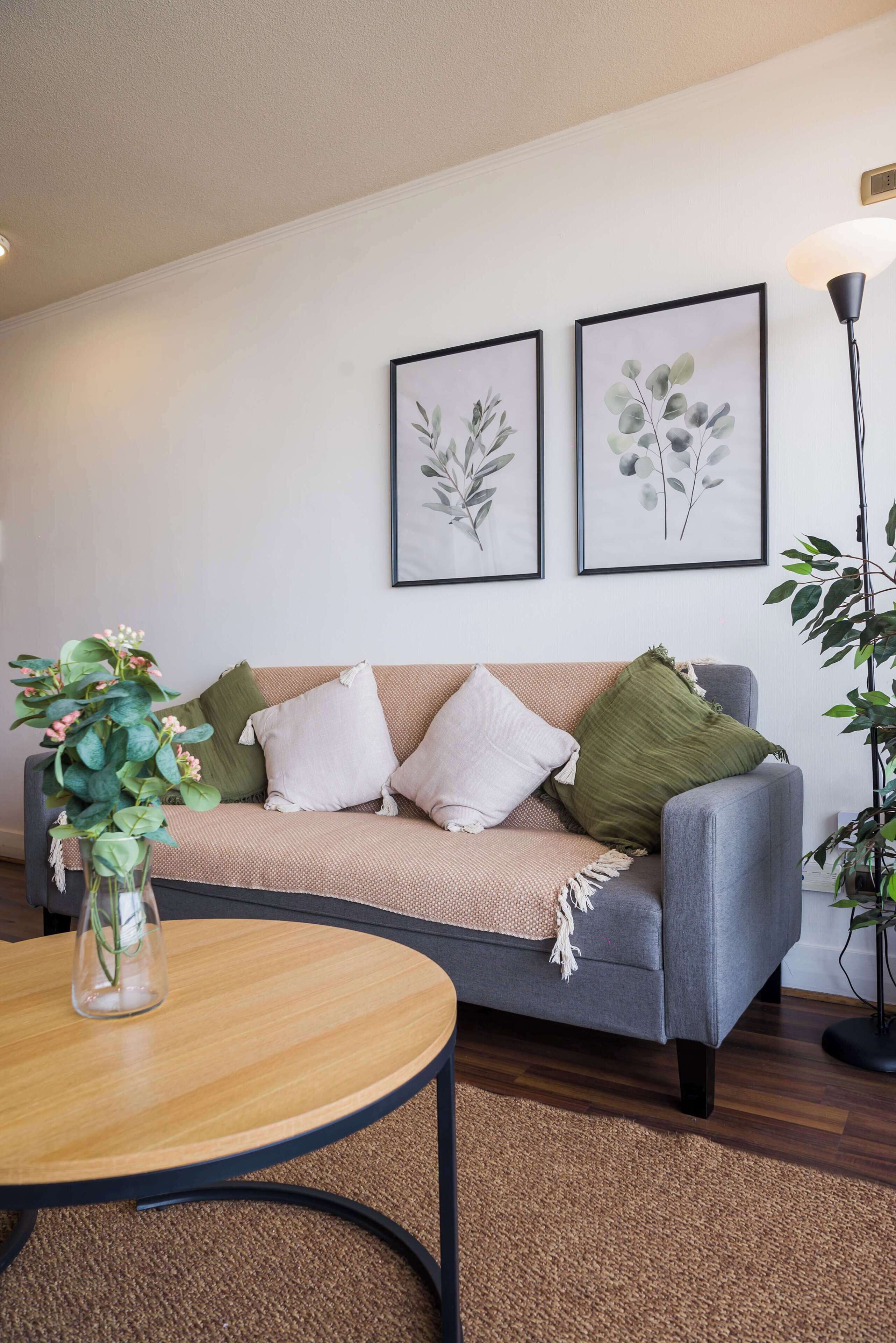 A living room with a grey sofa, a round wooden coffee table, and two framed botanical prints on the wall.