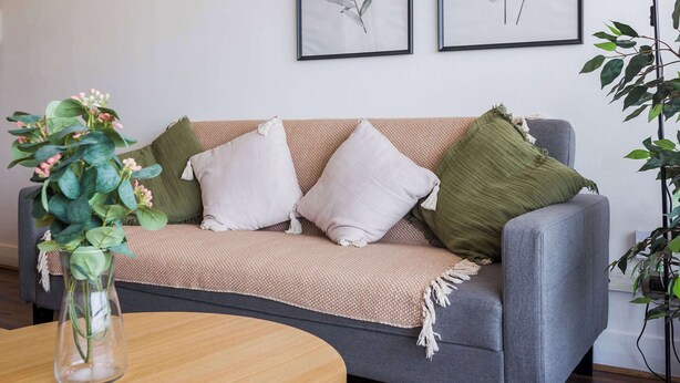 En stue med en grå sofa, et rundt træbord og to indrammede botaniske tryk på væggen.