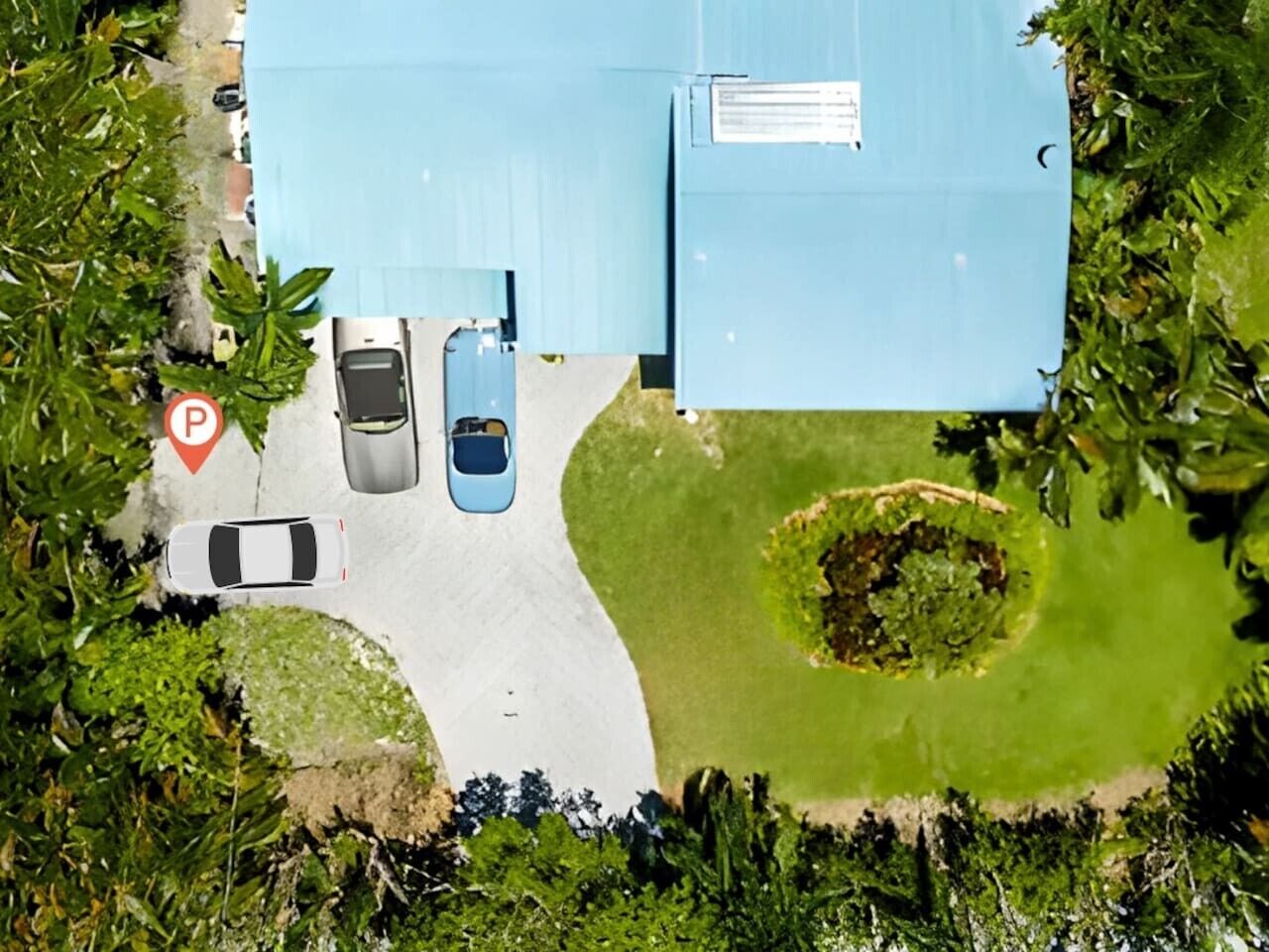 An aerial view of a building with a parking area, a blue roof, and surrounding greenery.