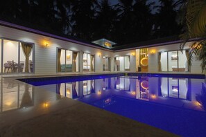 A modern house with a swimming pool, large windows, and a well-lit interior. - Serene Villa by iLiF Hotels (Alibag)