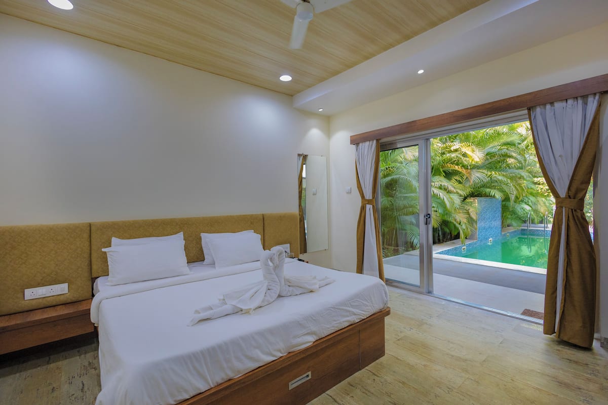 Quarto de hotel com cama, ventilador no teto, janela com cortinas e vista para uma piscina.