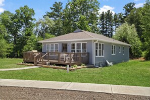 A small, single-story house with a deck, surrounded by a grassy yard and trees. - Beach front Cottage #3 in Lexington with AC, shared Hot Tub & Pool on Lake Huron (Lexington)