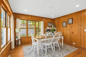 A dining area with a wooden table, white chairs, a rug, and a window with curtains.