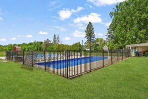A fenced swimming pool with a clear blue water feature, surrounded by well-maintained grass and trees. - Beach front Cottage #3 in Lexington with AC, shared Hot Tub & Pool on Lake Huron (Lexington)
