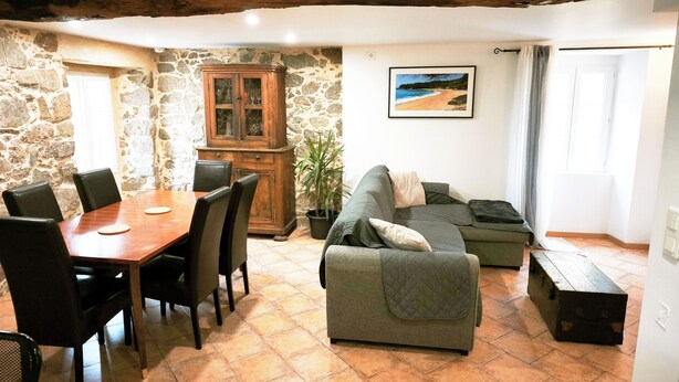 Un comedor con mesa y sillas de madera, pared de piedra, un armario, sofá y un cuadro en la pared.