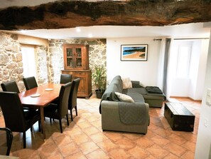 Un comedor con mesa y sillas de madera, pared de piedra, un armario, sofá y un cuadro en la pared.