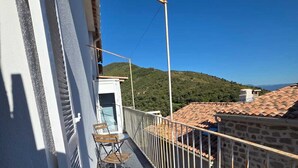 Un balcón con barandilla de metal, una pequeña mesa con sillas y vistas a una colina.