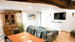 Un comedor con mesa y sillas de madera, pared de piedra, televisor y sofá.