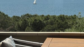 A view of the sea with a sailboat, a wooden deck, and a mountainous landscape in the background. - NEREIDS-The Coastal Suite. The sea one breath away from you (Quartu Sant'Elena)