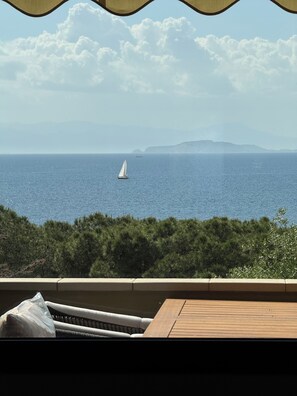 Vista del mar con un velero, una cubierta de madera y un paisaje montañoso al fondo.