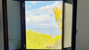 A room with a bed, a window with an open view of trees and sky, and a bedside table with a lamp. - NEREIDS-The Coastal Suite. The sea one breath away from you (Quartu Sant'Elena)