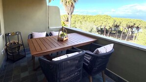A balcony with a wooden table and wicker chairs, a hanging light fixture, and a view of a green landscape. - NEREIDS-The Coastal Suite. The sea one breath away from you (Quartu Sant'Elena)