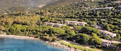 Una zona costera con edificios rodeados de vegetación exuberante y montañas al fondo.