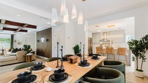 A modern dining area with a long wooden table, black dinnerware, and green upholstered chairs.