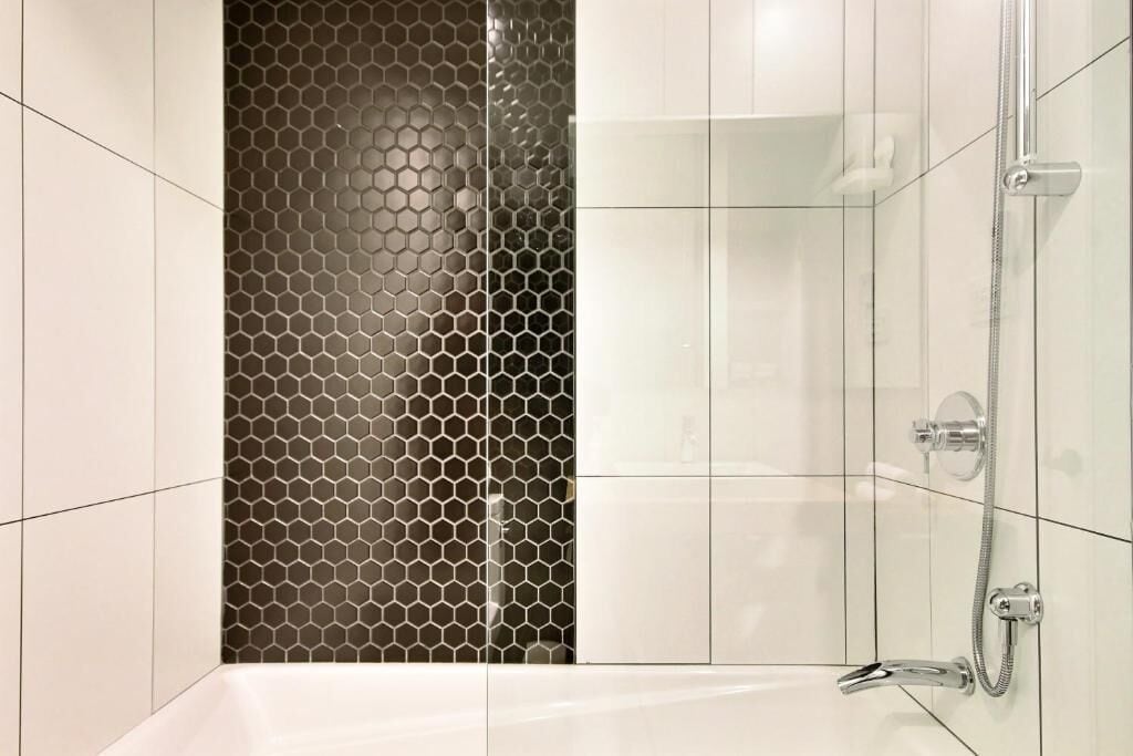 Een moderne badkamer met een douche, betegelde wanden en een glazen scheidingswand met een honingraatmotief.