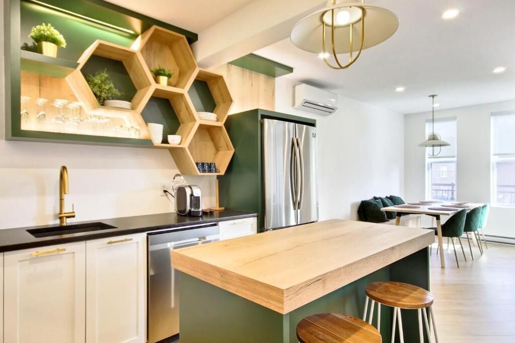 A modern kitchen with a central island, wooden shelves, a refrigerator, and a dining area with chairs.