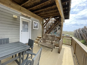 Eine Holzterrasse mit Tisch und Stühlen, eine Treppe und Blick auf den Strand.