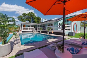Ein Swimmingpool mit weißem Zaun, Liegestühlen und einem orangefarbenen Sonnenschirm.