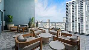 Eine Dachterrasse mit Sitzgelegenheiten und Topfpflanzen, einem Fernseher und Blick auf die Stadt.