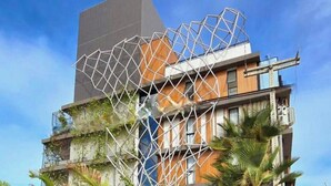 Ein modernes Gebäude mit einer geometrischen Fassade, einem markanten vertikalen Element und einem Balkon mit Pflanzen.