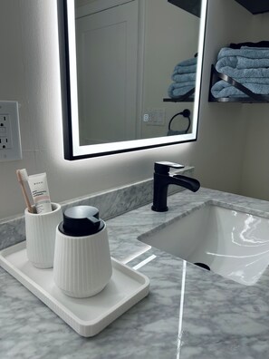 A bathroom with a white sink, black faucet, and a mirror with a light. There are toiletries on a tray. - Charming 2-bedroom apartment in amazing Dennis (Dennis)