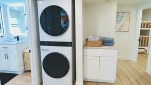 Un cuarto de lavandería con dos lavadoras y secadoras apiladas, un gabinete blanco con una cesta, y un cuadro en la pared.