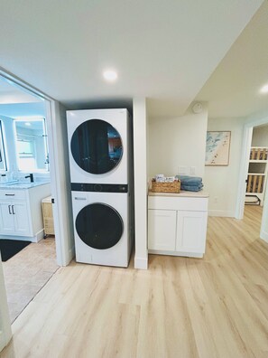 A laundry room with two stacked washers and dryers, a white cabinet with a basket, and a painting on the wall. - Charming 2-bedroom apartment in amazing Dennis (Dennis)