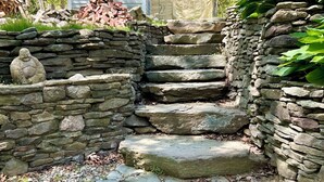 Una escalera de piedra que conduce a una casa, rodeada por un muro de piedra y follaje.