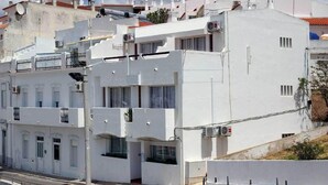 A multi-story building with balconies, air conditioning units, and a street in front. - APARTAMENTOS PESCADORES (Albufeira)