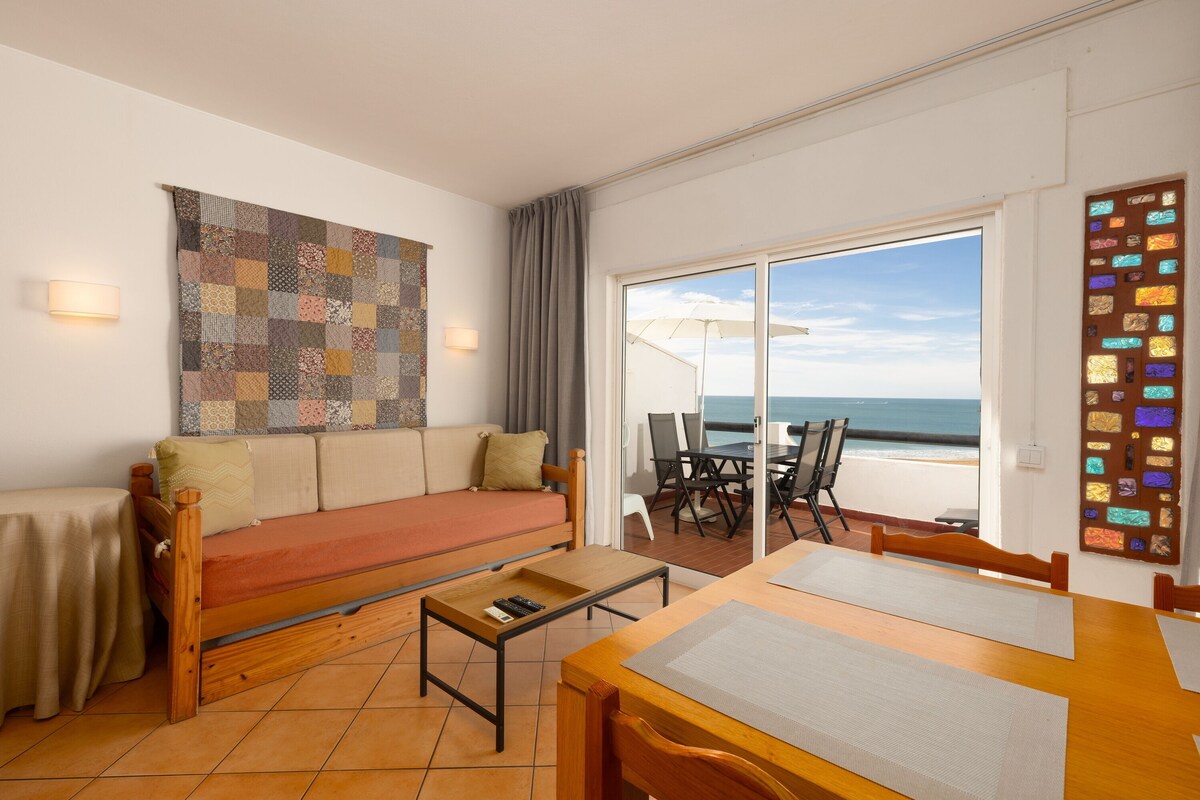 Ein Zimmer mit einer Couch, einem Tisch, Blick auf das Meer und einer farbenfrohen Wanddekoration.