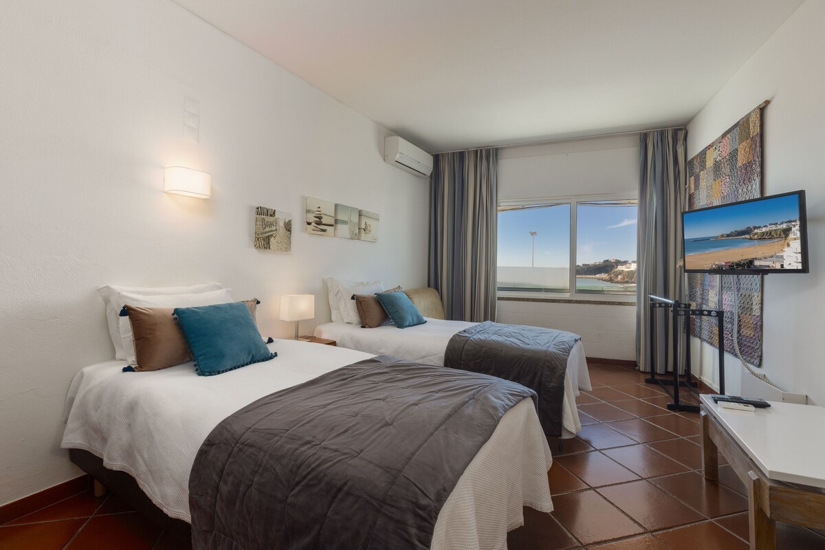 Ein Hotelzimmer mit zwei Betten, einem Fernseher, Kunstwerken an der Wand und einem Fenster mit Blick.