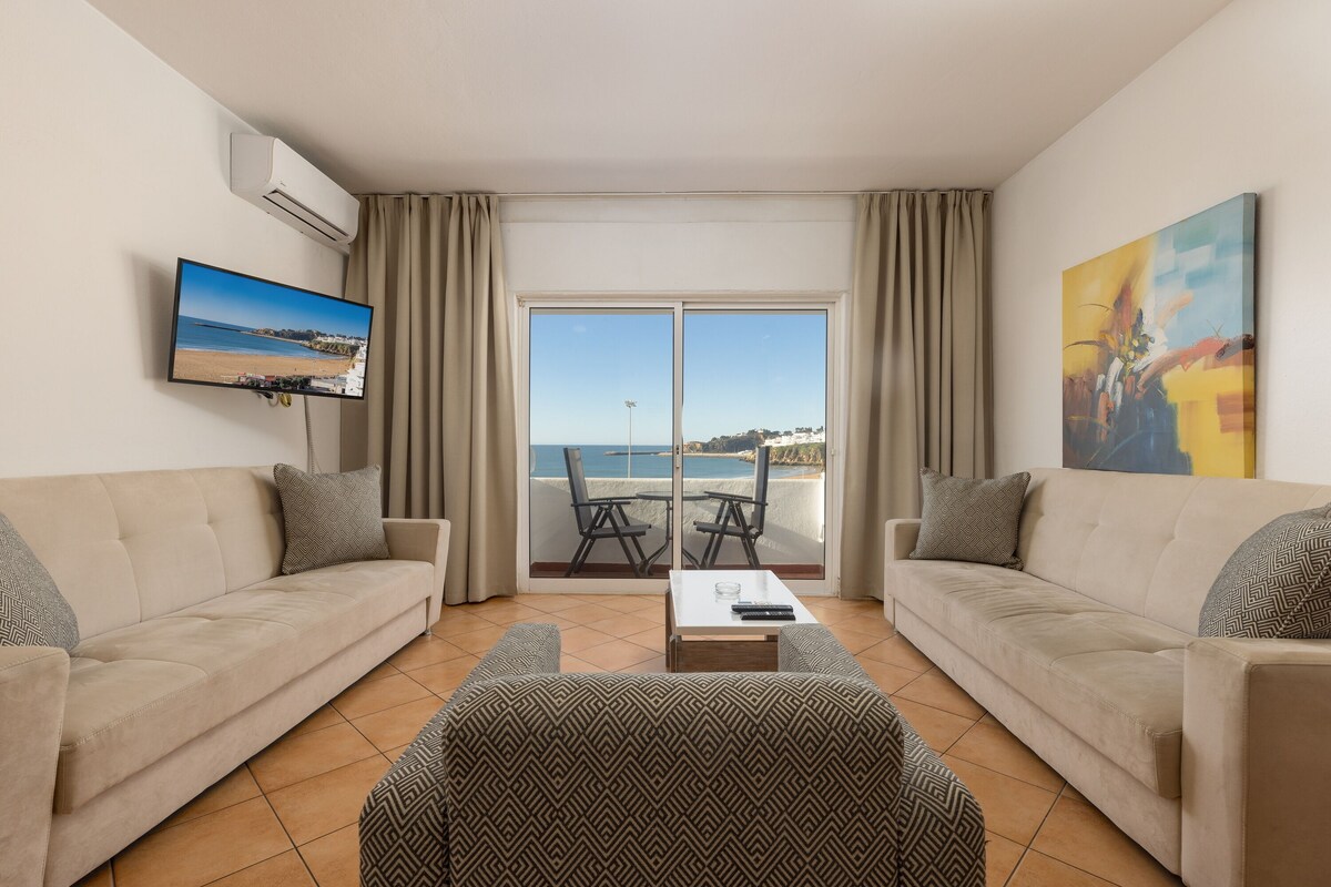 Ein Wohnzimmer mit zwei Sofas, einem Couchtisch, einem Fernseher und einem großen Fenster mit Meerblick.