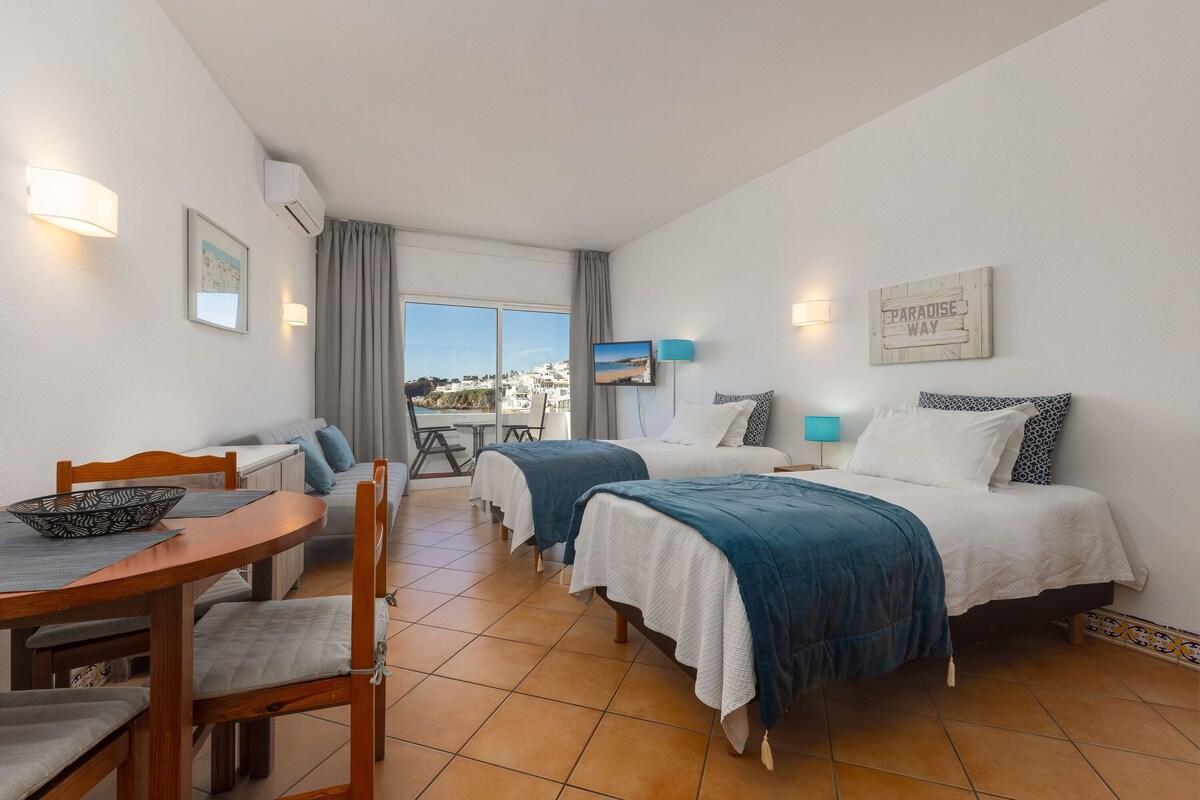 Ein Hotelzimmer mit zwei Betten, einem Esstisch, einem Fernseher und Blick auf die Stadt.
