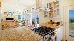 A modern kitchen with a gas stove, microwave, and a dining area with a view. - Cottage by the Sea (Whitethorn)