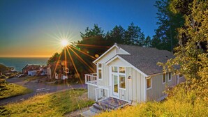 A coastal house with a front porch, a driveway, and a view of the ocean at sunset. - Cottage by the Sea (Whitethorn)