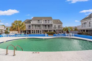 Ein Swimmingpool mit einer Markierung für eine Wassertiefe von etwa einem Meter, umgeben von Liegestühlen und einem Gebäude mit Balkonen.