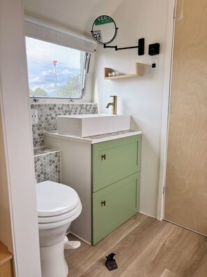 Ein kleines Badezimmer mit Toilette, einem Waschbecken mit goldfarbenem Wasserhahn, einem grünen Schrank und einem Spiegel an der Wand.