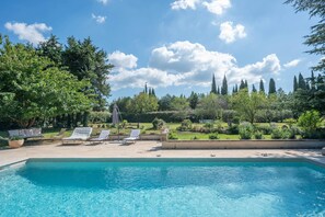 Piscina con sillones de descanso y vista al jardín.
