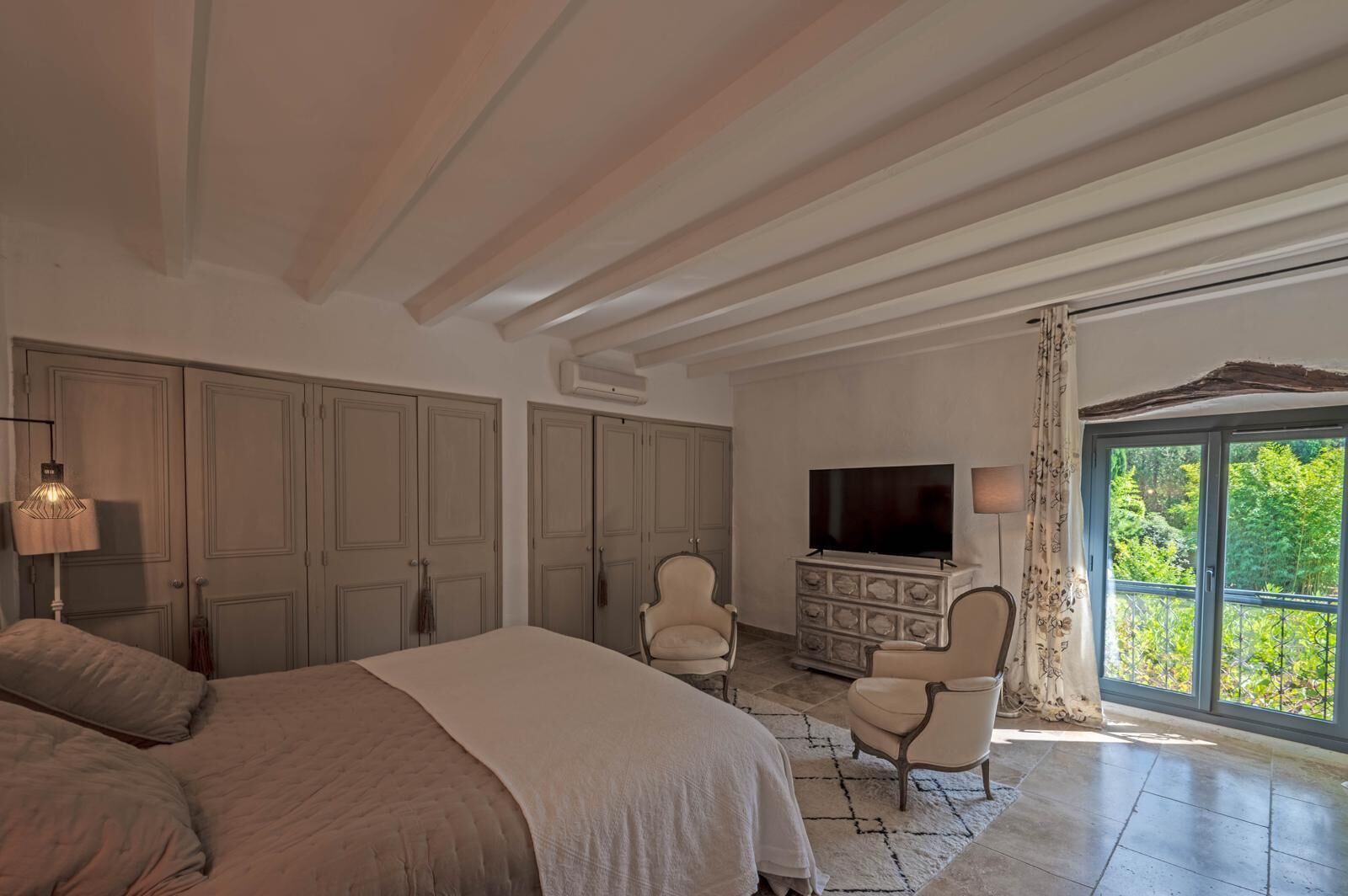 A bedroom with a large bed, two chairs, a TV, and a dresser.