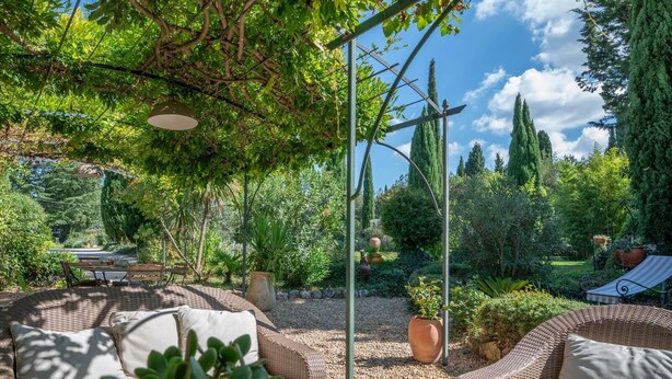 Eine Gartenpatio mit Korbmöbeln, einer Pergola und verschiedenen Pflanzen.