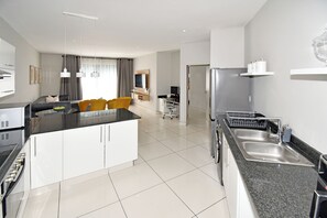 Eine moderne Küche mit einer zentralen Kochinsel, einem Essbereich mit gelben Stühlen, einem eingebauten Backofen und einem Kühlschrank.