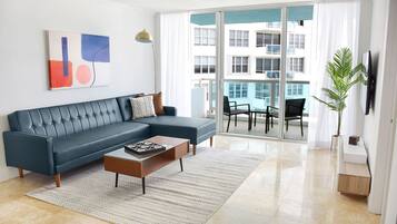 Una sala de estar moderna con un sofá seccional, una mesa de centro y un ventanal con vistas a un edificio.