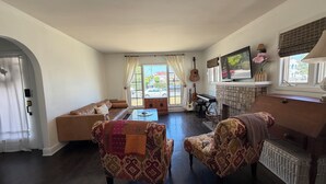 Ein Wohnzimmer mit einer Couch, gemusterten Sesseln, einem Couchtisch, einem Kamin, einem Fernseher und einem Klavier.