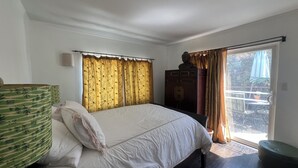 Ein Schlafzimmer mit einem Bett, Vorhängen, einem Kleiderschrank und Blick durch eine Schiebetür.